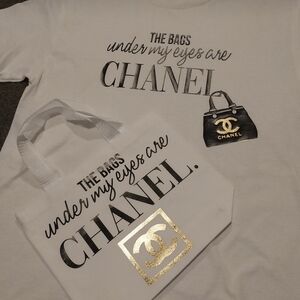 White Tee with Black and Gold Print That Says "The Bags Under My Eyes R Chanel.